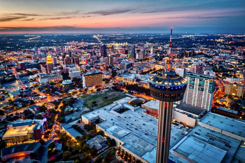 Aerial view of downtown San Antonio, Texas at night with rotating Tower of the Americas in foreground.